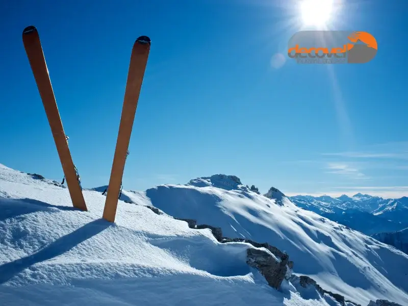 چوب اسکی فرو رفته در برف در نمای کوهستان برفی. آموزش اسکی با دکوول